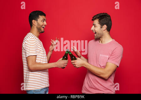 Deux jeunes hommes gais isolés sur fond rouge, de boire l'eau de soude à partir de bouteilles Banque D'Images