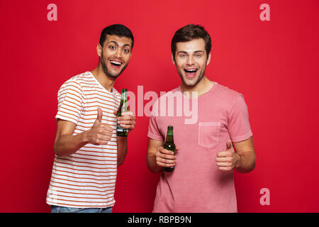 Deux jeunes hommes gais isolés sur fond rouge, de boire l'eau de soude à partir de bouteilles, Thumbs up Banque D'Images