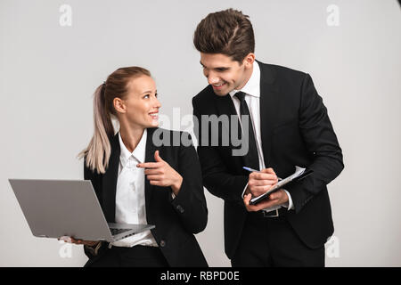 Smiling business couple wearing isolés convient sur fond gris, en travaillant avec un ordinateur portable, la prise de notes Banque D'Images