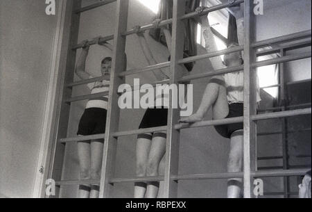 Années 1950, historiques, écolières dans vêtements de sport à l'école secondaire du comté sur une piscine d'escalade en bois à une classe PE, England, UK. Banque D'Images