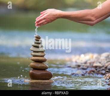 Close-up résumé image de femme part verser de l'eau sur les différentes tailles inégales brun naturel et la forme des pierres comme équilibrée pile pyramide monument Banque D'Images