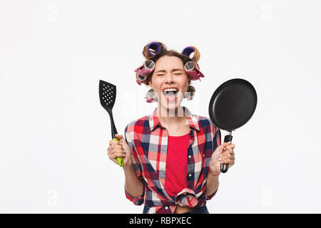 Femme au foyer en colère avec des bigoudis dans les cheveux isolés sur fond blanc, holding poêle Banque D'Images