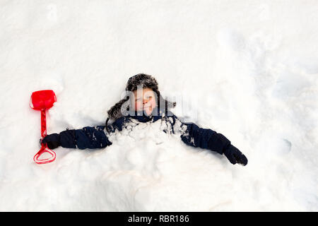 Journée d'hiver, beaucoup de neige, l'enfant enterré lui-même avec une pelle pour enfants autour du cou dans la neige. Banque D'Images