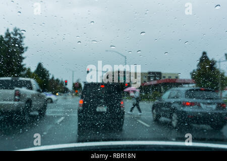 Gouttes de pluie sur le pare-brise en roulant sur un jour de pluie, un parapluie rose avec des piétons traversant la rue en arrière-plan, arrière-plan flou ; C Banque D'Images