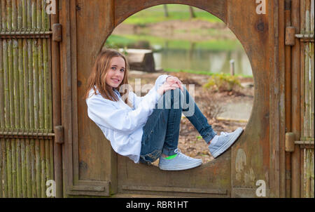 Posant pour l'appareil photo d'une jeune fille portant un sweat et un jean se trouve dans un cadre en bambou situé dans un parc public. Banque D'Images