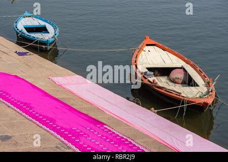 Deux bateaux sur le Gange au soleil avec deux longues dhotis ou séchage sari sur le pavé à l'avant-plan : photo prise à Varanasi, Inde Banque D'Images