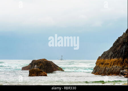 Un bateau de pêche peut être vu dans le brouillard au-delà des roches intertidales le long de Seal Rock Beach sur la côte de l'Oregon. Banque D'Images