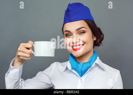 Jeune femme hôtesse de l'air professionnels isolés sur mur gris holding tasse de thé chaud close-up à la caméra smiling happy Banque D'Images