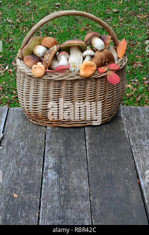 Différents types de champignons comestibles dans un panier en osier sur une vieille table en chêne, avec copie espace Banque D'Images