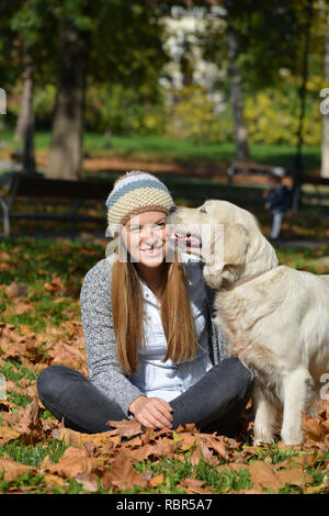 Cute blonde fille assise sur les feuilles d'automne dans un parc avec son chien, orientation verticale Banque D'Images