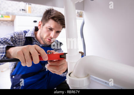 Jeune homme Plumber Repairing Sink tuyau avec une clé réglable Banque D'Images