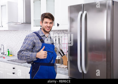 Portrait de technicien Gesturing Thumbs Up en face de réfrigérateur Banque D'Images