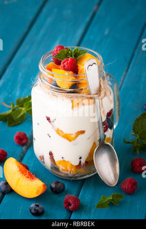 Fruits et baies dessert dans un pot Mason sur tableau bleu. Salade de fruits avec du yogourt ou de la crème fraîche. Banque D'Images