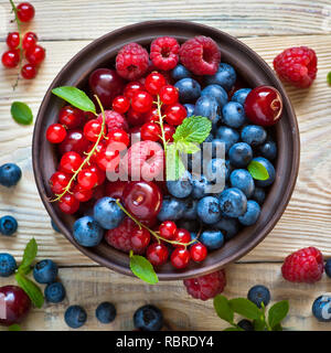 Les baies fraîches. Divers petits fruits d'été dans un bol sur la table en bois rustique. Banque D'Images