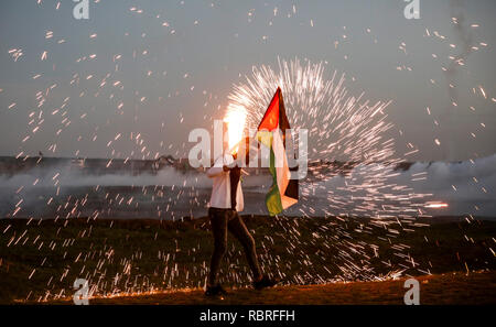 Manifestant palestinien vu tenant un drapeau pendant les affrontements avec les forces israéliennes suite à une manifestation le long de la frontière avec Israël à l'est de la ville de Gaza. Banque D'Images