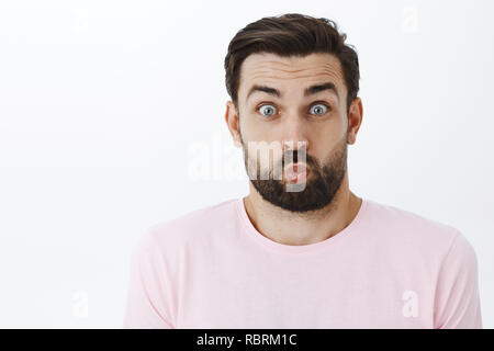 Close-up shot de drôle et enfantin ludique jeune papa dupant autour de jouer avec les enfants et d'élever les sourcils lèvres pliage, popping yeux à huis clos comme singeant l'amusement sur fond gris Banque D'Images