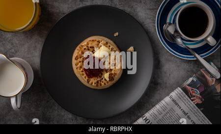 Bon matin petit-déjeuner avec télévision lay crumpet beurrée, confiture de fraises, du café noir, jus d'orange et un papier de nouvelles Banque D'Images