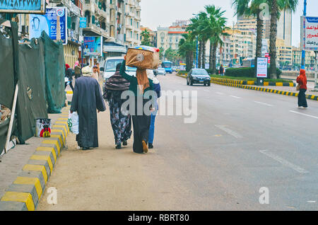 Alexandrie, Egypte - Décembre 19, 2017 : Le groupe de sections locales promenades le long de la route en corniche Avenue, jeune femme porte le sac sur sa tête, sur Décembre 20 01 Banque D'Images