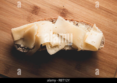 Sandwich avec du beurre et du fromage dur sur une tranche de pain de seigle fraîchement cuits sur une planche à découper en bois Banque D'Images