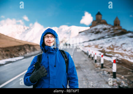 Stepantsminda Gergeti, Géorgie). Photographe Voyageur Backpacker touristiques homme posant près de l'église Holy Trinity - Tsminda Sameba. Belle Lan Géorgienne Banque D'Images