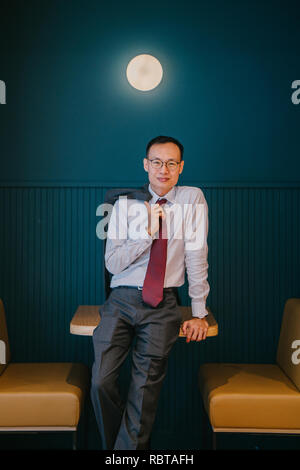 Portrait d'un homme d'affaires Asiatique ou professionnel (avocat, banquier, etc.) appuyé contre une table dans son bureau. Il est grand, mince et confiant. Banque D'Images