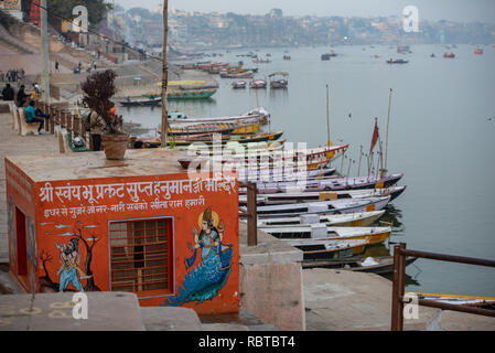 Vue générale du Gange le long des Ghats de Varanasi, en Inde avec un petit temple de couleur orange à l'avant-plan et de bateaux dans l'arrière-plan. Banque D'Images