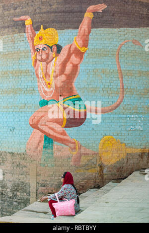 Une fresque murale peinte sur un réservoir d'eau, de l'Hindou Hanuman le Dieu Singe avec une femme assise sur les marches en face du Gange Ghat de Varanasi, Inde Banque D'Images