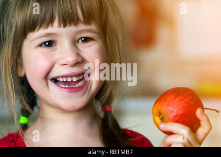 Une jolie petite fille de papier frisé sourit et est titulaire d'une pomme rouge. Portrait d'un bébé heureux de manger une pomme rouge. L'enfant perd des dents de lait. L'alimentation saine Banque D'Images