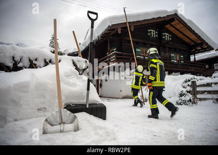 Berchtesgaden, Allemagne. Jan 12, 2019 : pelles est debout devant des pompiers qui ne sont que l'élimination d'un toit de neige. Les fortes chutes de neige des derniers jours, continuer à maintenir les services d'urgence dans le sud de la Bavière et de nouvelle neige est déjà proche. Selon les autorités, plus de 1 000 personnes ont été déployés dans les districts du sud de la Haute-Bavière. Photo : Lino Mirgeler/dpa Banque D'Images