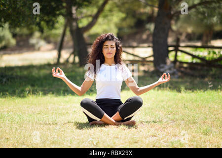 Jeune femme arabe faisant du yoga dans la nature. Le port de l'Afrique du Nord vêtements sport lotus faisant figure de parc urbain. Banque D'Images