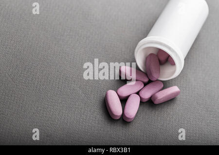 Grand pilules roses versé d'un récipient en plastique sur fond noir Banque D'Images