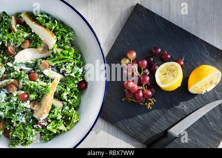 Vue de dessus de tranches de citrons et de raisins sur un bloc d'ardoise à côté d'une assiette de salade de poulet Banque D'Images