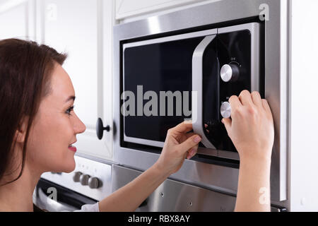 Vue latérale d'une jeune femme à l'aide d'un four micro-ondes four dans la cuisine Banque D'Images