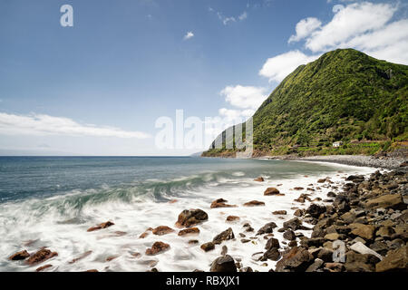 Plage de Lonely avec de grands rochers, une vague roule, mouvement de l'eau dans une longue exposition, sommet de montagne à la végétation luxuriante dans l'arrière-plan, l'effet de profondeur - Banque D'Images