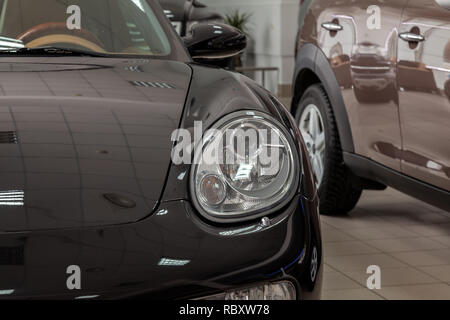 Vue rapprochée de la face avant d'une voiture de sport noire dans un coupé avec un phare rond transparent dans l'affaire lors de l'exposition. Banque D'Images