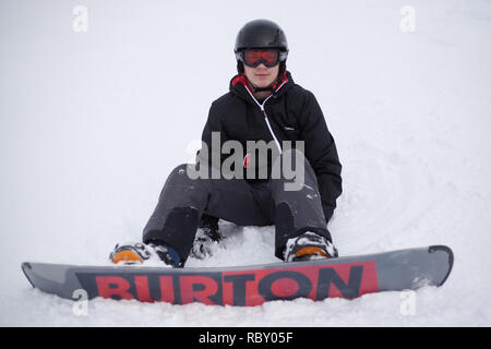 Snowboarder garçon assis sur la neige sur la pente. Banque D'Images