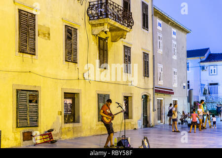 Un musicien de rue (musicien ambulant) en face de d'un vieux bâtiment traditionnel dans la vieille ville de Krk, l'île de Krk, Kvarner, Croatie Banque D'Images