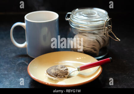 Un bleu mug, un pot de thé en sachets d'une soucoupe, cuillère à café et un sachet de thé utilisé sur un plan de travail de cuisine. Banque D'Images