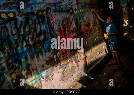 Un apprenti peintre signe colombien met la colle sur le mur griffonnée sur le signe de l'atelier de peinture à Cartagena, Colombie. Banque D'Images