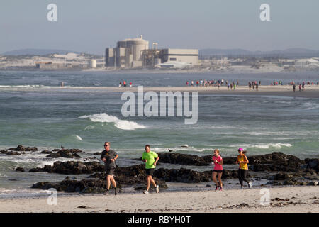 Parkrun jogging sur la plage à Melkbosstrand avec Centrale Koeberg en arrière-plan. Parkrun est un mouvement mondial de Samedi 5km s'exécute en dehors. Banque D'Images