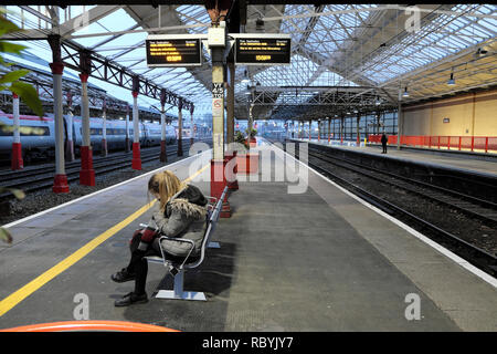 Une jeune femme assise sur un banc en attente d'un train sur la plate-forme à la gare de Crewe en Angleterre KATHY DEWITT Banque D'Images