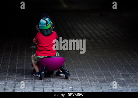 Une photo d'un enfant dans un chandail rouge roulant assis sur un plasma violet voiture comme ride sur toy à la recherche dans l'obscurité Banque D'Images