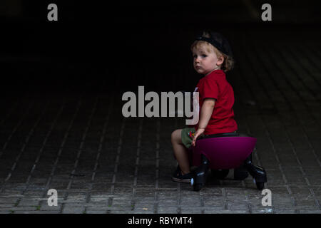 Une photo d'un enfant dans un chandail rouge roulant assis sur un plasma violet voiture comme ride sur toy à la recherche dans l'obscurité Banque D'Images