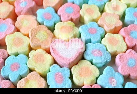 Seulement un en forme de coeur rose et blanc entre les tas de guimauve en forme de fleur de couleur pastel Candies Banque D'Images