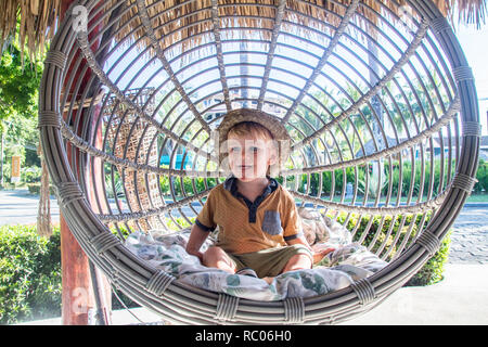 Un portrait d'un jeune garçon avec un chapeau heureusement assis dans un joli jardin balançoire Banque D'Images