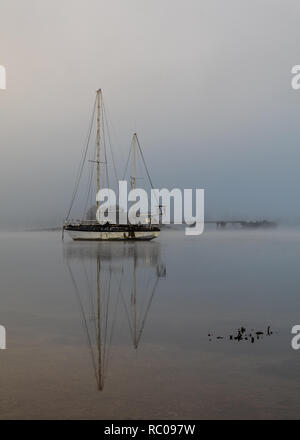 Bateau solitaire au milieu du lac sur le côté de tôt le matin jusqu'au nord de Fort William en Ecosse . Dim et brumeuse avec humeur réflexions étonnantes. Banque D'Images