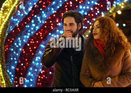 Date pour la Saint-Valentin. Guy et petite amie de marche dans les rues de night city. La tendresse et les soins. Lumières de fête en arrière-plan. Banque D'Images