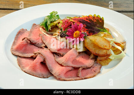 Roastbeef mit Bratkartoffeln, dekoriert und mit Kräutern essbaren Blüten | rôti de boeuf rôti avec pommes de terre frites ou Banque D'Images