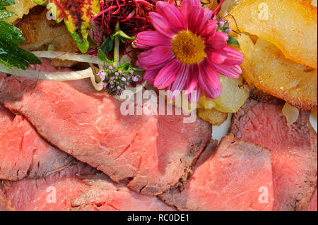 Roastbeef mit Bratkartoffeln, dekoriert und mit Kräutern essbaren Blüten | rôti de boeuf rôti avec pommes de terre frites ou Banque D'Images