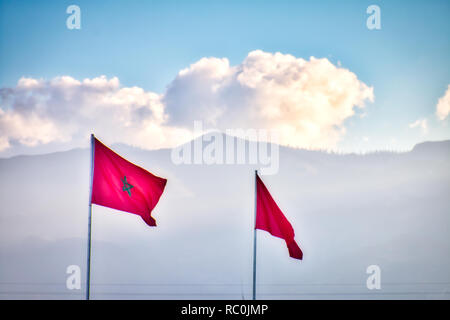 Brandissant des drapeaux du Maroc dans le vent avec un fond de montagnes et nuages Banque D'Images